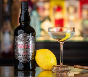 Black Triple Six gin bottle on the bar with lemon and a coupe glass next to it.